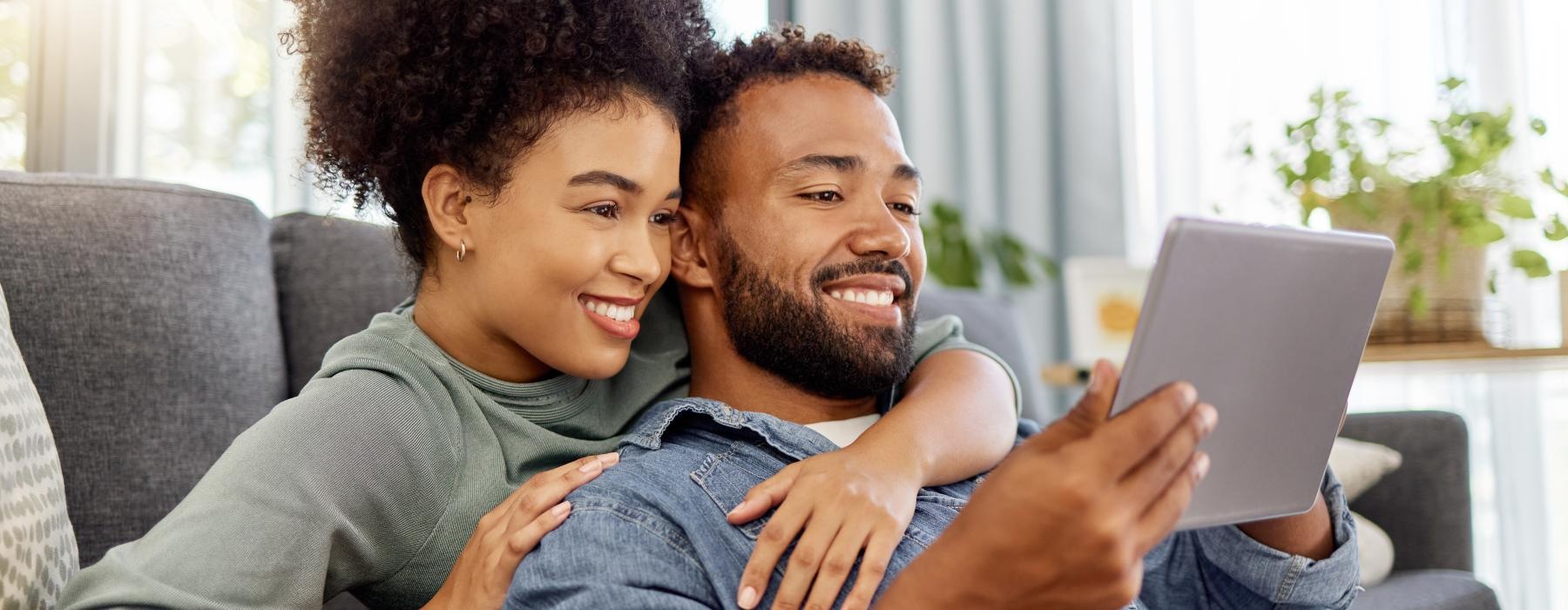 a man and a woman sitting on a couch looking at a laptop